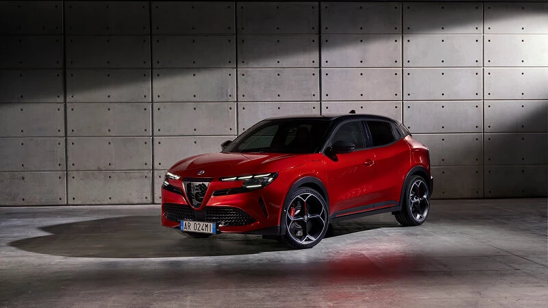 Červené Alfa Romeo Junior s čiernou strechou zaparkované pred betónovou stenou v štúdiu