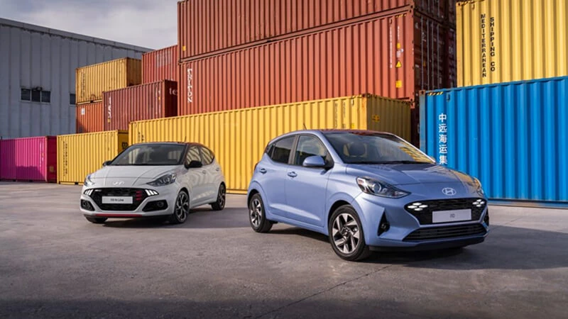 Modrý Hyundai i10 a biely Hyundai i10 N Line stojace vedľa seba v kontajnerovom prístave