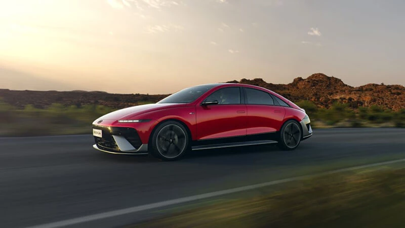 Červený Hyundai Ioniq 6 v jazde po ceste krajinou pri západe slnka, bočný pohľad