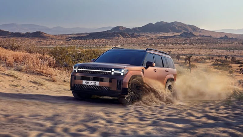 Medený Hyundai Santa Fe v jazde po piesočnatej púštnej ceste so zvíreným prachom