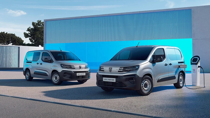 Nový Peugeot Partner v dvoch dĺžkach karosérie – strieborné dodávky, vpravo elektrický E-Partner pri nabíjacej stanici